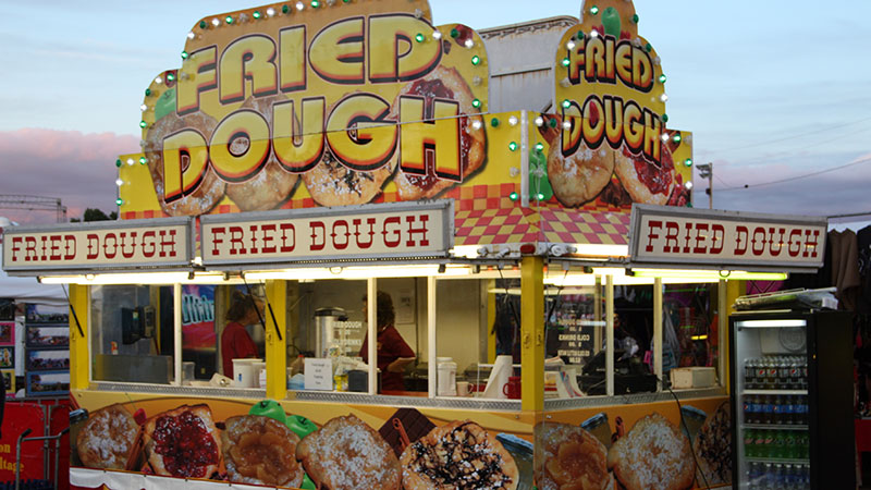 A colorful food kiosk decorated with photos of Fried Dough and lit up with many white and green lights